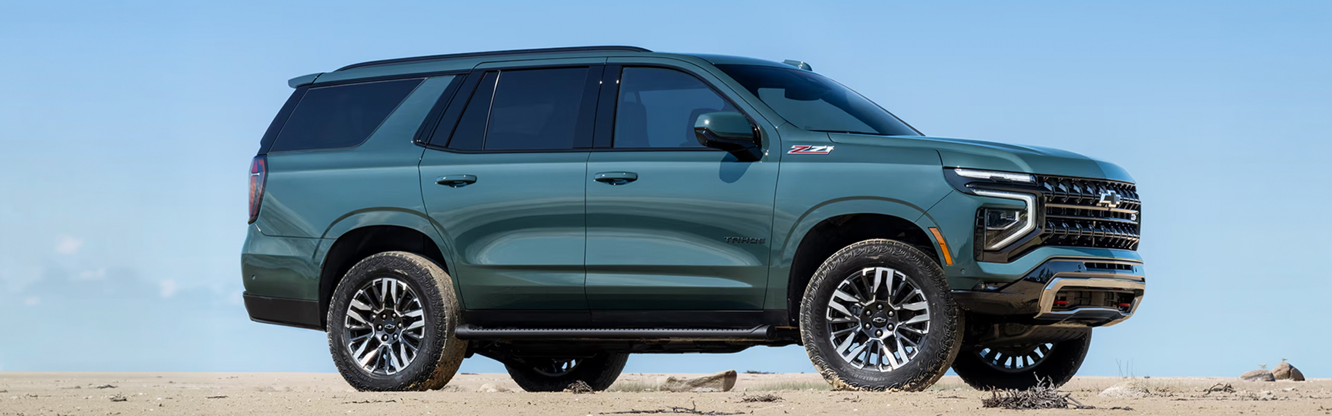 2026 Chevrolet Tahoe SUV in teal parked on a sandy surface under a clear blue sky.
