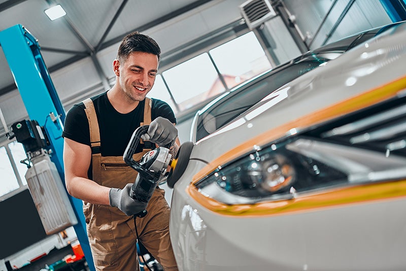 Auto technician polishing a car headlight in service center