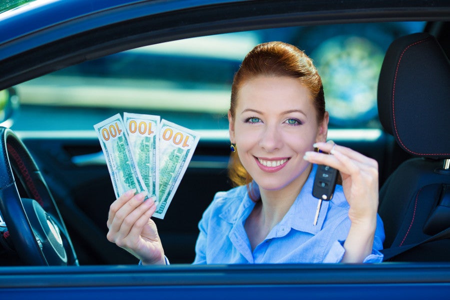 A woman inside her car, holding cash in her left hand and a car key in another